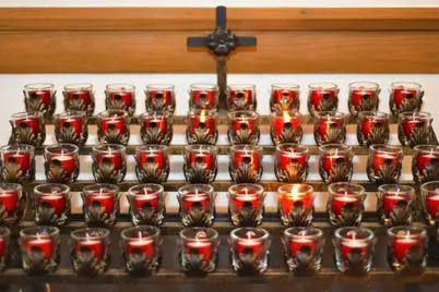 Many lit votive candles by cross.